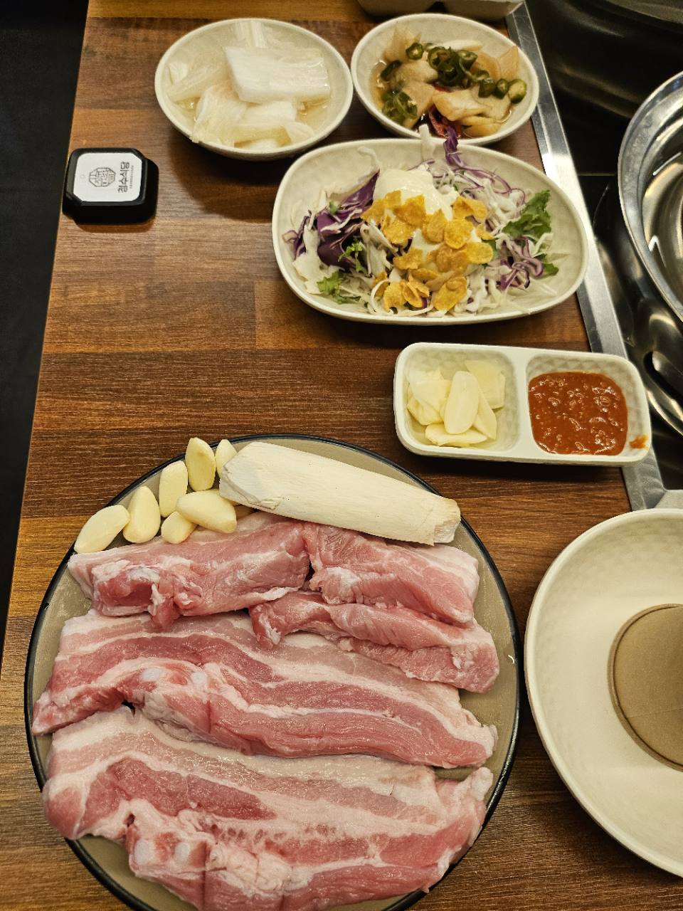 삼겹살 접시와 마늘, 샐러드와 절임류가 놓인 청수식당 상차림